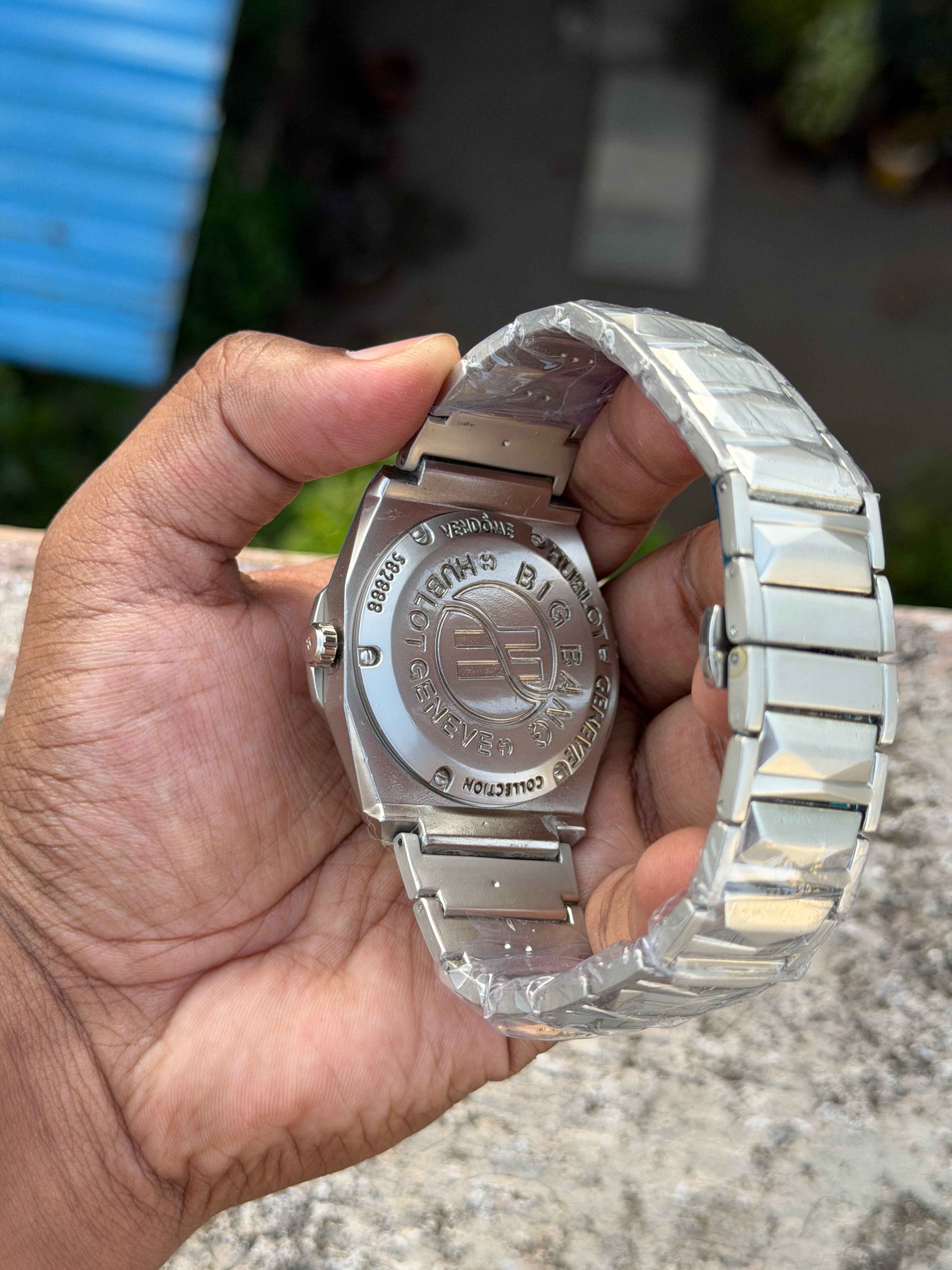 Hublot-style watch with a silver-tone stainless steel integrated bracelet and black dial.