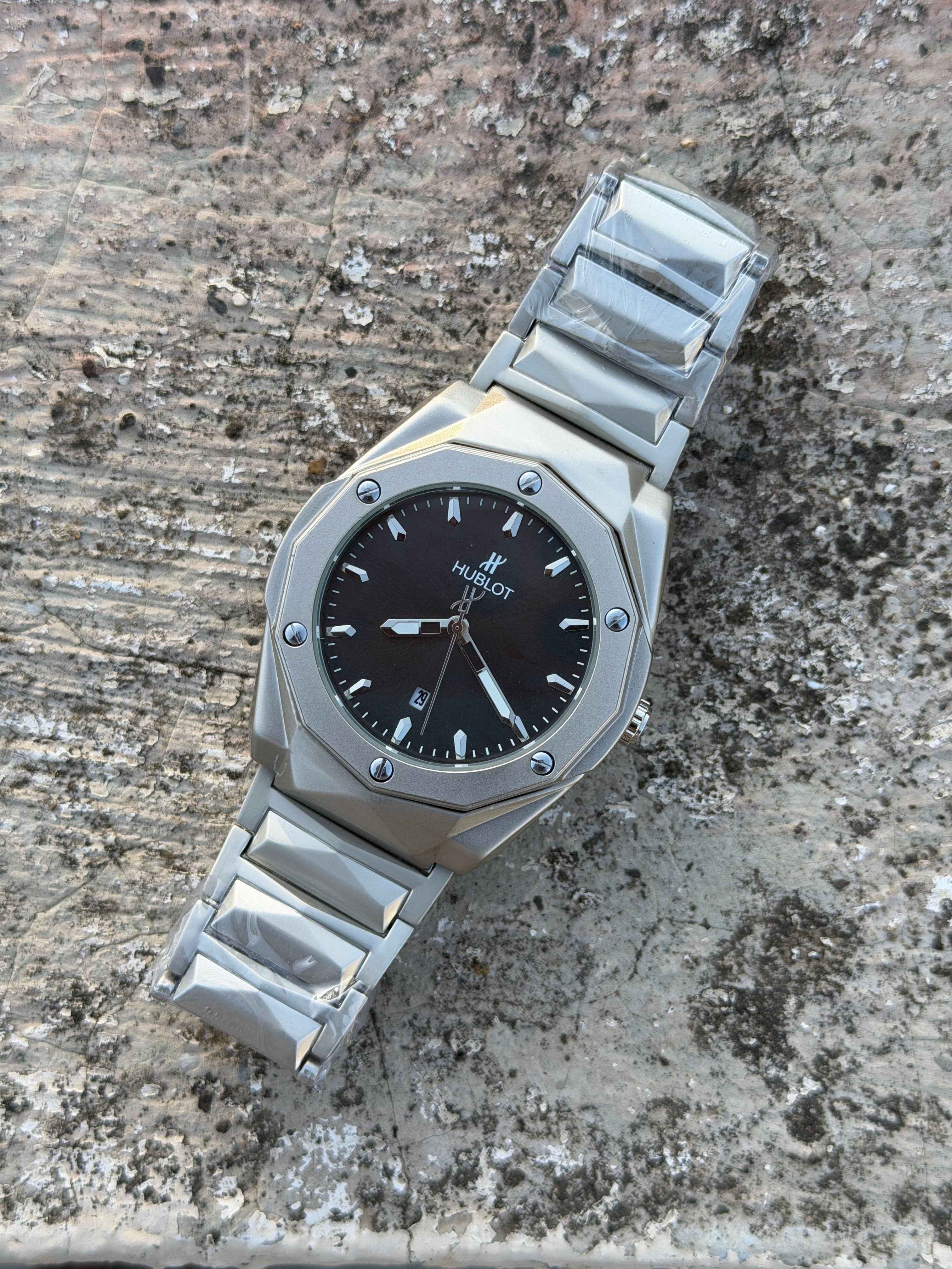 Hublot-style watch with a silver-tone stainless steel integrated bracelet and black dial.